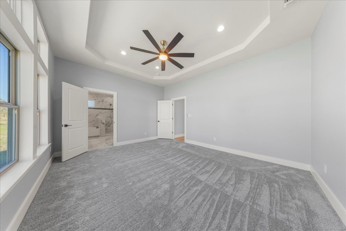 217 Gato Road Cedar Creek, TX 78612 - Photo 23 of 39 Unfurnished bedroom with a tray ceiling, ceiling fan, ensuite bathroom, recessed lighting, and carpet