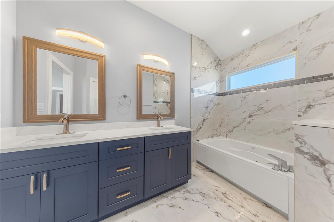 217 Gato Road Cedar Creek, TX 78612 - Photo 26 of 39 Full bath featuring double vanity, a tub with marble appearance, light marble finish floors, lofted ceiling, and recessed lighting