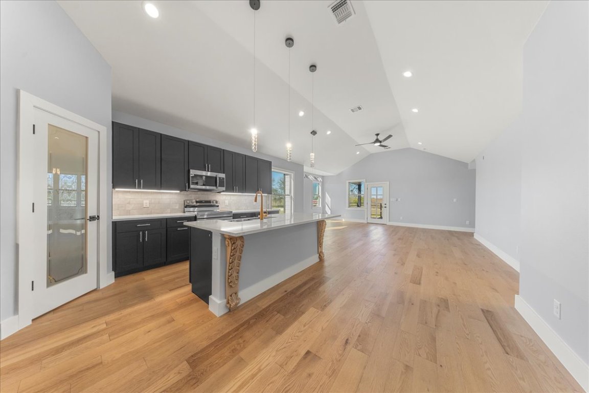 217 Gato Road Cedar Creek, TX 78612 - Photo 38 of 39 Kitchen with decorative light fixtures, dark cabinets, open floor plan, lofted ceiling, and an island with sink