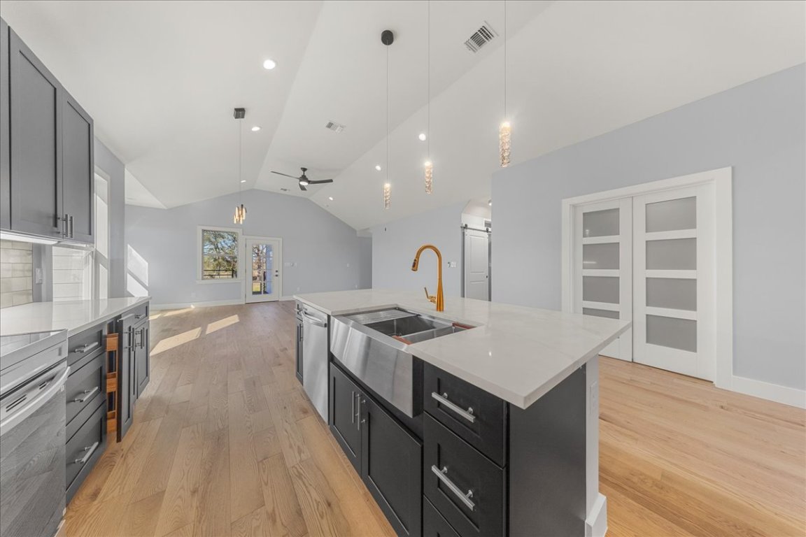 217 Gato Road Cedar Creek, TX 78612 - Photo 8 of 39 Kitchen with dark cabinets, pendant lighting, lofted ceiling, light wood-style floors, and light stone counters
