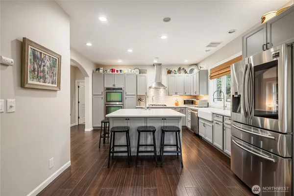 a kitchen with stainless steel appliances granite countertop a refrigerator a stove a sink dishwasher and white cabinets with wooden floor