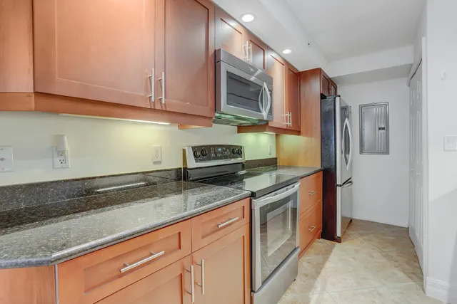 a kitchen with stainless steel appliances granite countertop a sink a stove and a refrigerator with wooden cabinets