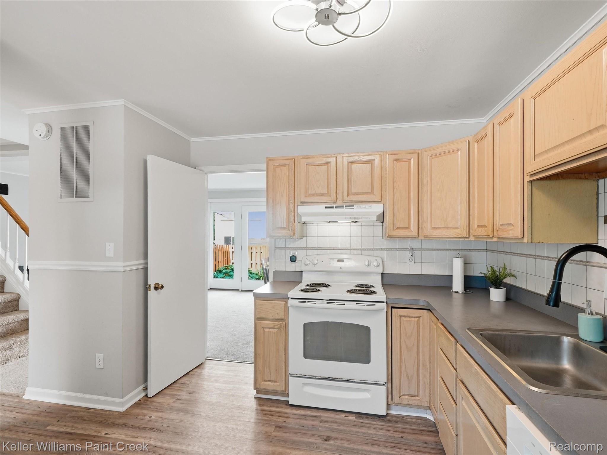 1208 Lear Court Rochester, MI 48307 - Photo 8 of 28 Kitchen featuring light wood cabinetry, white tile backsplash, a stainless steel sink, and wood-finish flooring