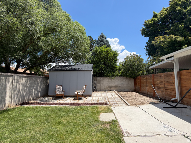 375 East 10560 South Sandy, UT 84070 - Photo 18 of 21 Expansive backyard featuring a manicured lawn, concrete patio, and a storage shed with a shingled roof