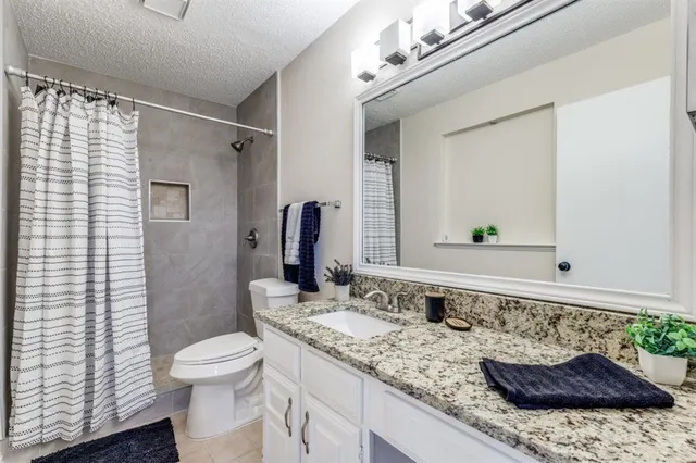 a bathroom with a granite countertop sink a toilet a mirror and shower