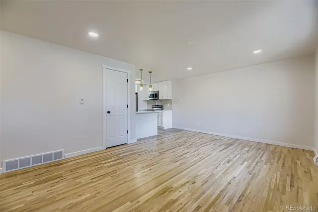 a view of empty room with wooden floor and kitchen