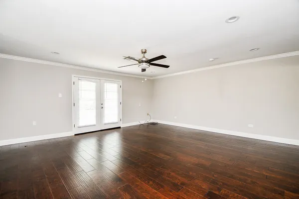 a view of an empty room with wooden floor and a ceiling fan