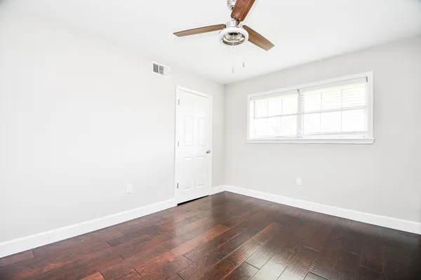 an empty room with wooden floor fan and windows
