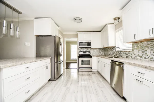 a kitchen with granite countertop a refrigerator oven a sink dishwasher and white cabinets with wooden floor