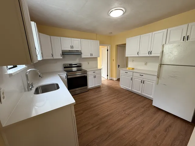 a kitchen with granite countertop a sink a stove a refrigerator and white cabinets