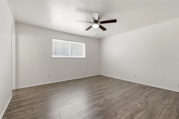 an empty room with wooden floor fan and windows