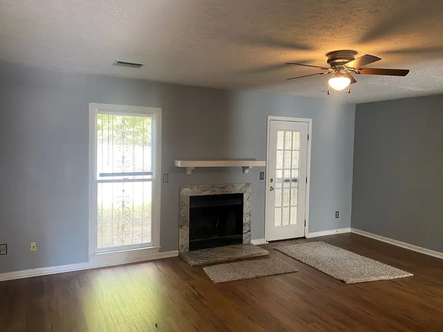 a view of an empty room with wooden floor fireplace and a window
