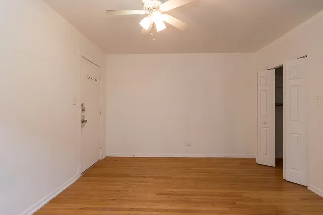 a view of an empty room with wooden floor and a ceiling fan