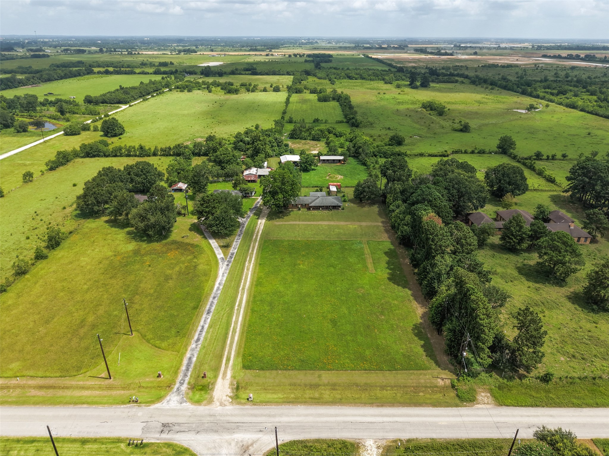 34366 Owens Road Hempstead, TX 77445 - Photo 22 of 46 Elevated aerial view showcasing the full property layout, including the home, open pasture, mature trees, and generous road frontage in a peaceful country setting