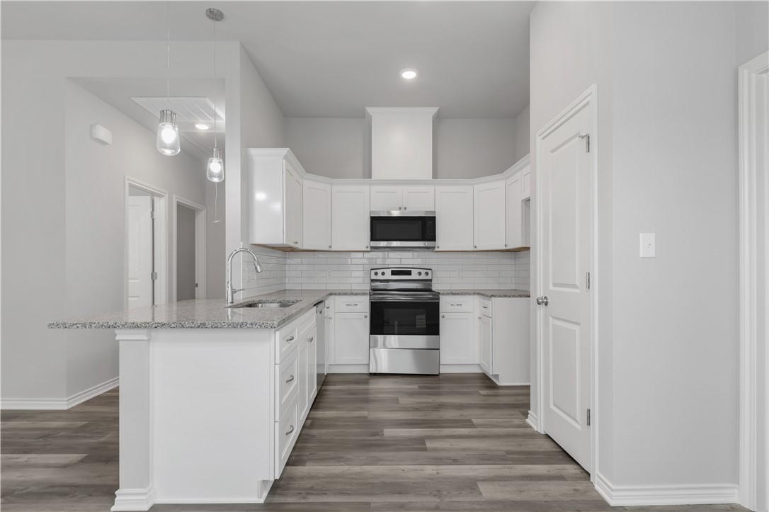 1805 Pin Oak Street Bryan, TX 77803 - Photo 10 of 20 Kitchen featuring appliances with stainless steel finishes, light stone countertops, a peninsula, wood finished floors, and tasteful backsplash