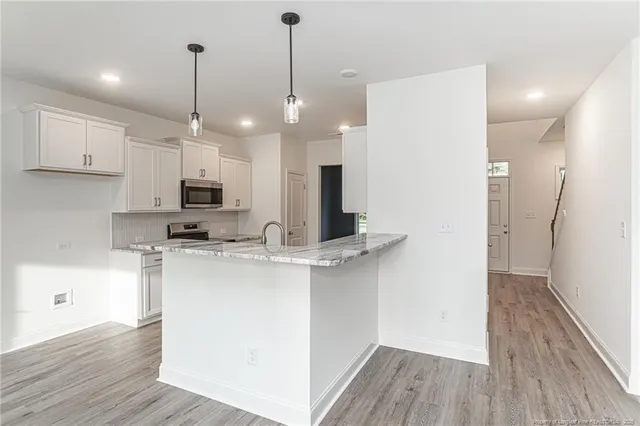 a kitchen with stainless steel appliances kitchen island a refrigerator a sink dishwasher a stove and white cabinets with wooden floor