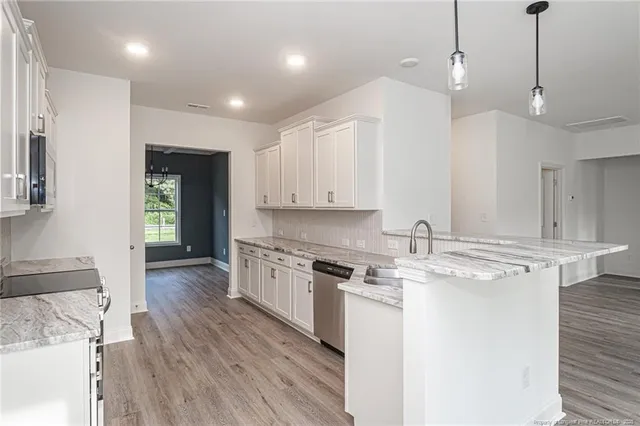 a kitchen with stainless steel appliances granite countertop a sink a stove a refrigerator and white cabinets with wooden floor