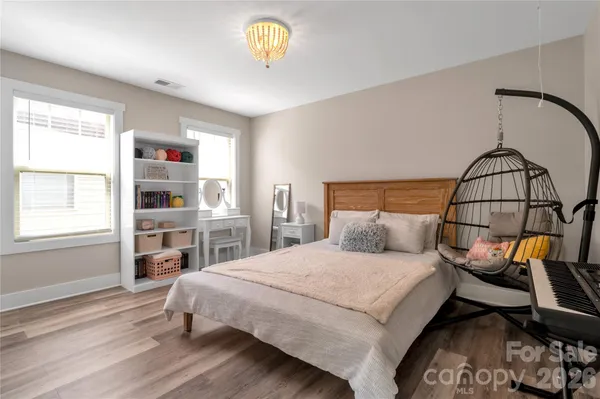 a bedroom with a bed a dresser and potted plants with the wooden floor