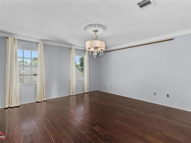 an empty room with wooden floor chandelier and windows