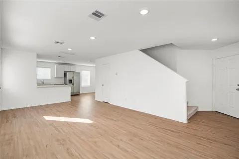 a view of an empty room with wooden floor and a kitchen