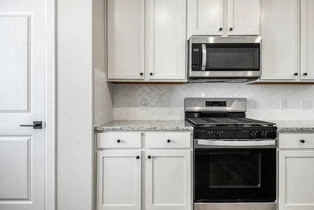 a kitchen with stainless steel appliances granite countertop white cabinets a stove top oven