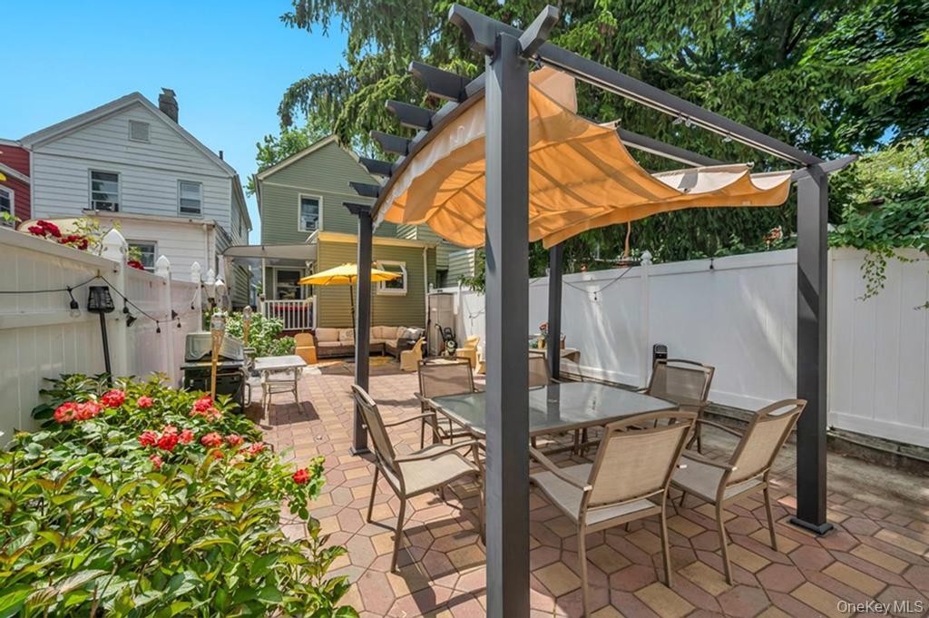 89-13 84th Street Queens, NY 11421 - Photo 7 of 34 Paved patio featuring a pergola with a retractable fabric shade, surrounded by lush landscaping and privacy fencing