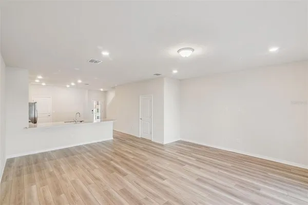 a view of an empty room with wooden floor and kitchen