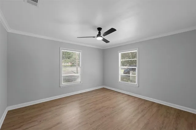 an empty room with wooden floor ceiling fan and windows