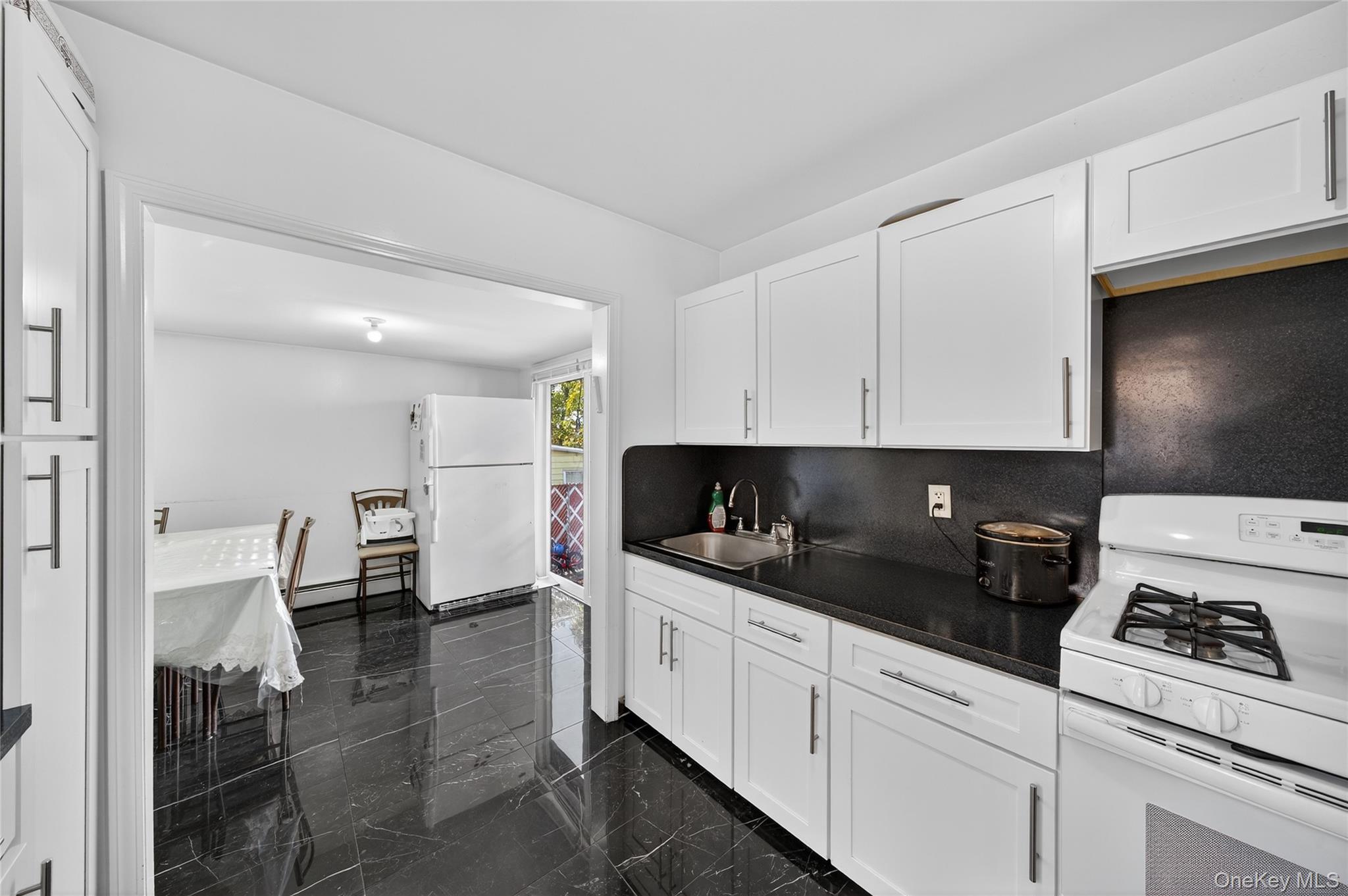 469 Hillside Road Monroe, NY 10950 - Photo 7 of 44 Kitchen with white appliances, dark countertops, white cabinetry, a baseboard heating unit, and backsplash