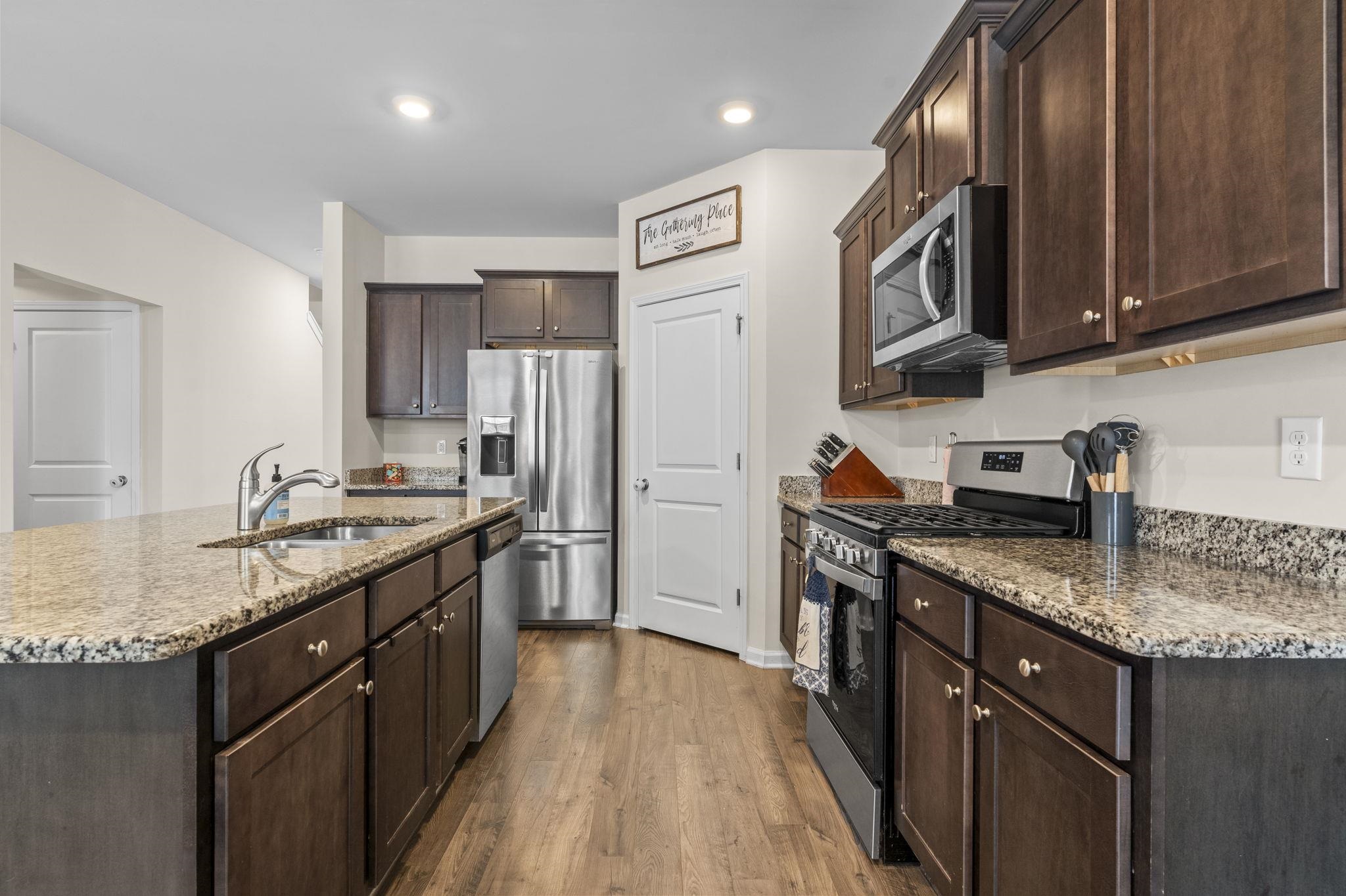 2605 Muhly Court Conway, SC 29526 - Photo 6 of 33 Kitchen featuring appliances with stainless steel finishes, dark brown cabinets, dark wood finished floors, a kitchen island with sink, and light stone counters