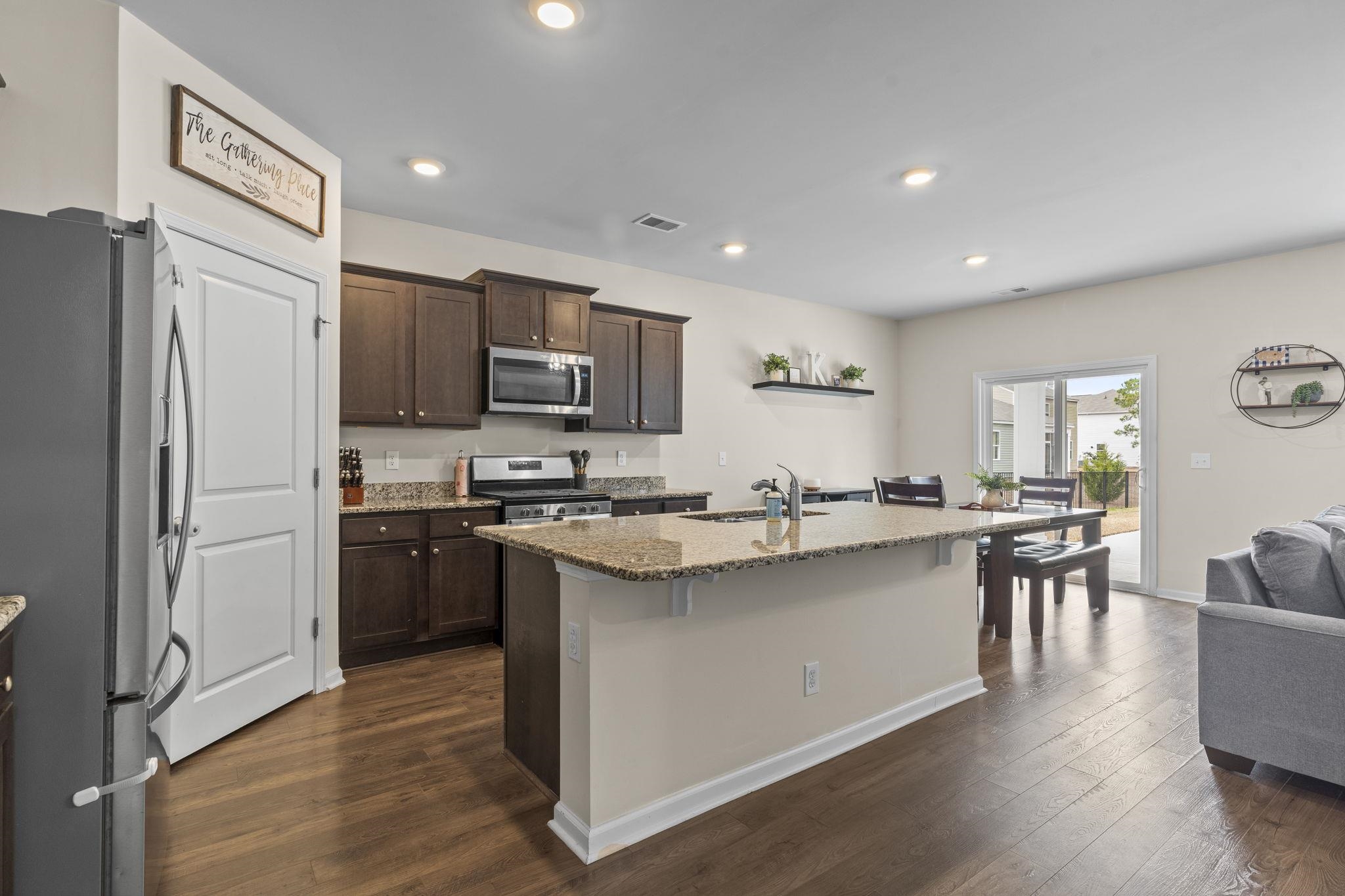 2605 Muhly Court Conway, SC 29526 - Photo 7 of 33 Kitchen featuring dark brown cabinets, appliances with stainless steel finishes, light stone countertops, a center island with sink, and recessed lighting