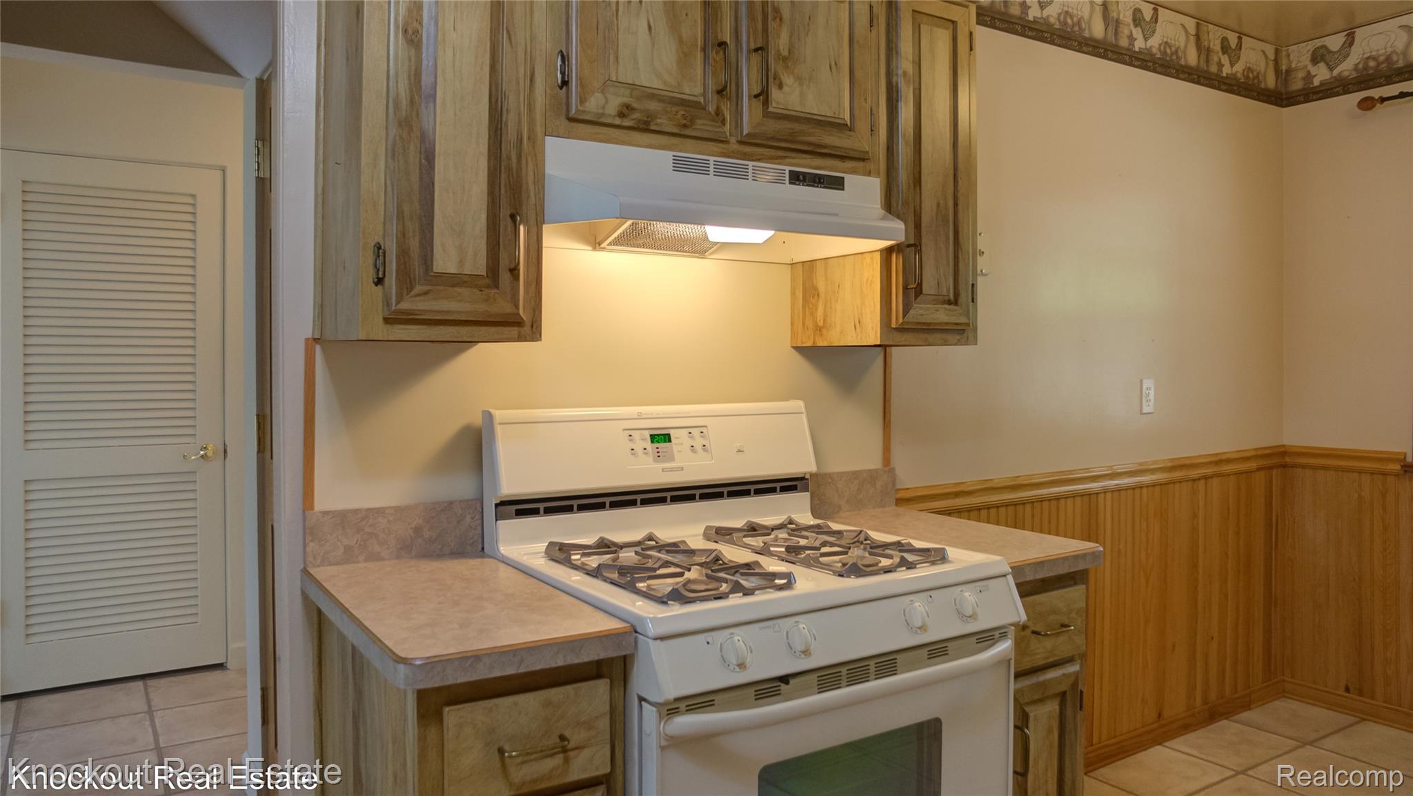 4465 Dirker Road Saginaw, MI 48638 - Photo 19 of 56 Kitchen with white gas range, light tile patterned floors, light countertops, a wainscoted wall, and wood finish cabinetry