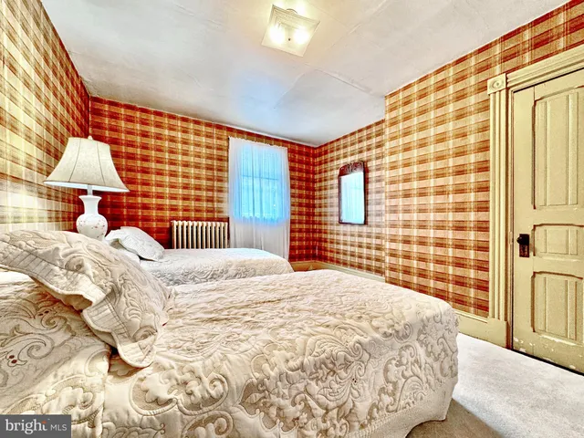 a bedroom with a bed and a lamp on dresser next to a window