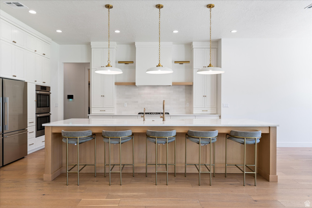 1192 East Corral Way Washington, UT 84780 - Photo 16 of 81 Expansive kitchen featuring a large central island with seating, stainless steel appliances, abundant white cabinetry, light wood-finish flooring, and pendant lighting