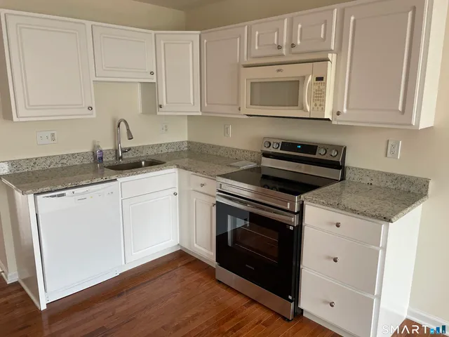 a kitchen with granite countertop white cabinets and a stove a oven with wooden floor