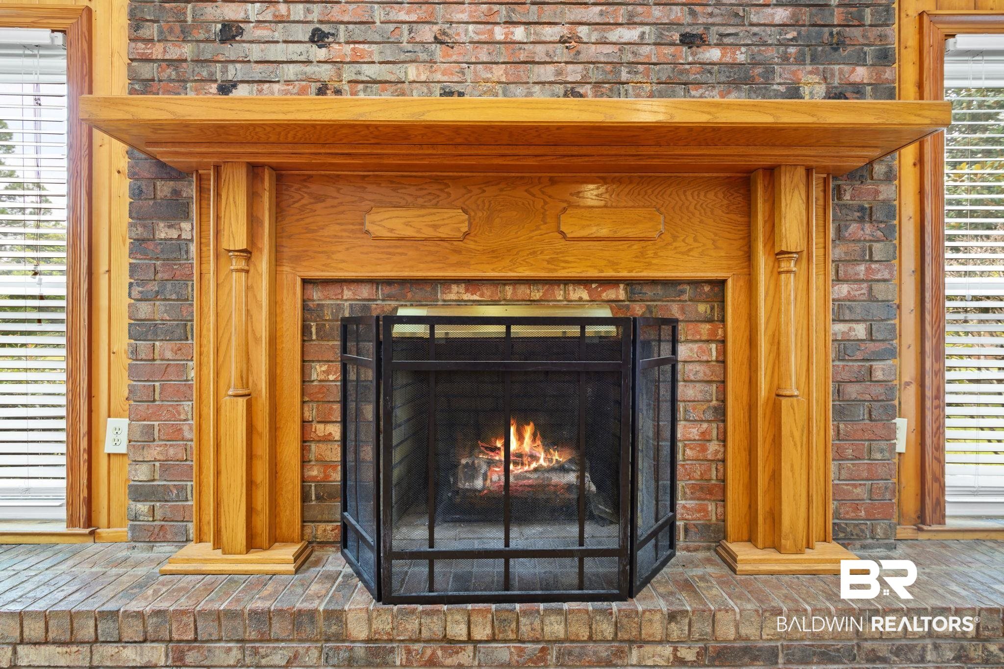 7540 2 Mile Road Irvington, AL 36544 - Photo 16 of 82 Brick fireplace with a wood mantel and decorative pillars, featuring a raised hearth and metal fire screen