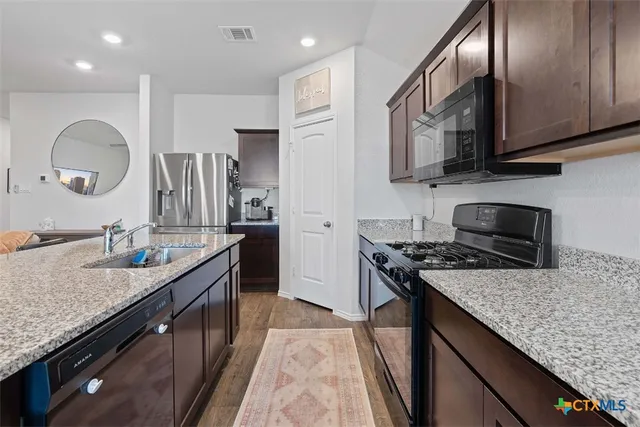 a kitchen with granite countertop stainless steel appliances a sink stove top oven and cabinets