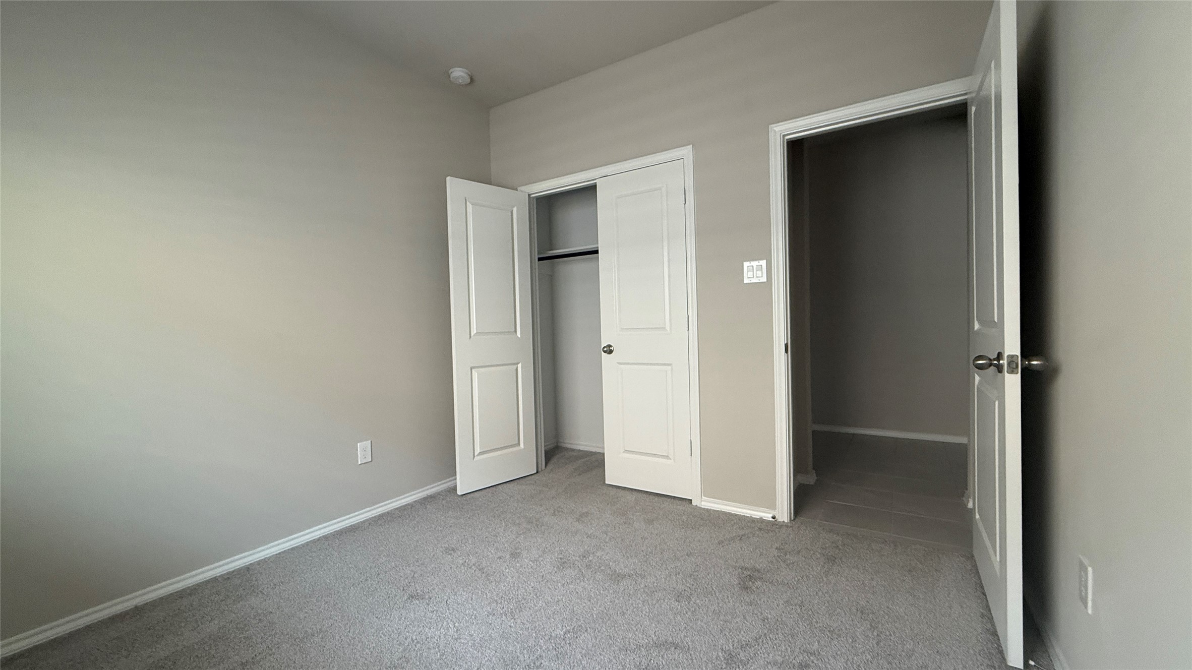 31961 Retama Rnch Drive Spring, TX 77386 - Photo 9 of 25 This photo shows a bright, neutral-toned bedroom with carpeted flooring, featuring a double-door closet and an adjacent hallway.