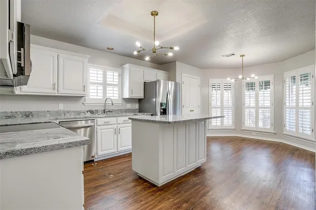 a kitchen with granite countertop a stove a sink dishwasher a refrigerator and white cabinets with wooden floor