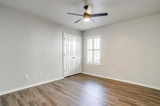 an empty room with wooden floor ceiling fan and windows