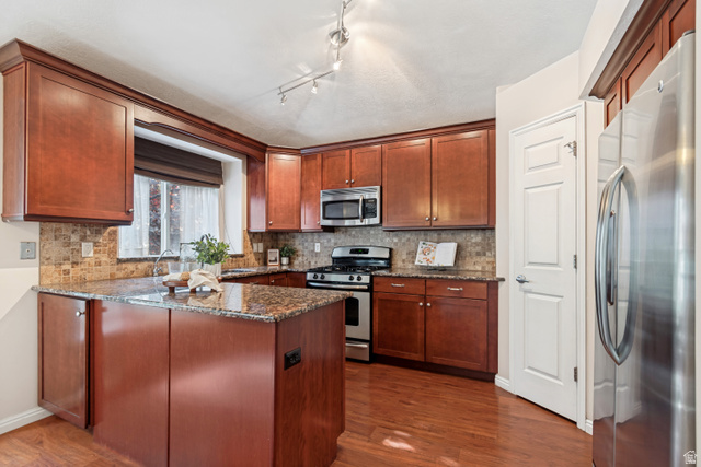 11798 Spiraea Way Draper, UT 84020 - Photo 6 of 21 Kitchen featuring rich wood cabinetry, stone countertops, a tiled backsplash, stainless steel appliances, and wood-finish flooring