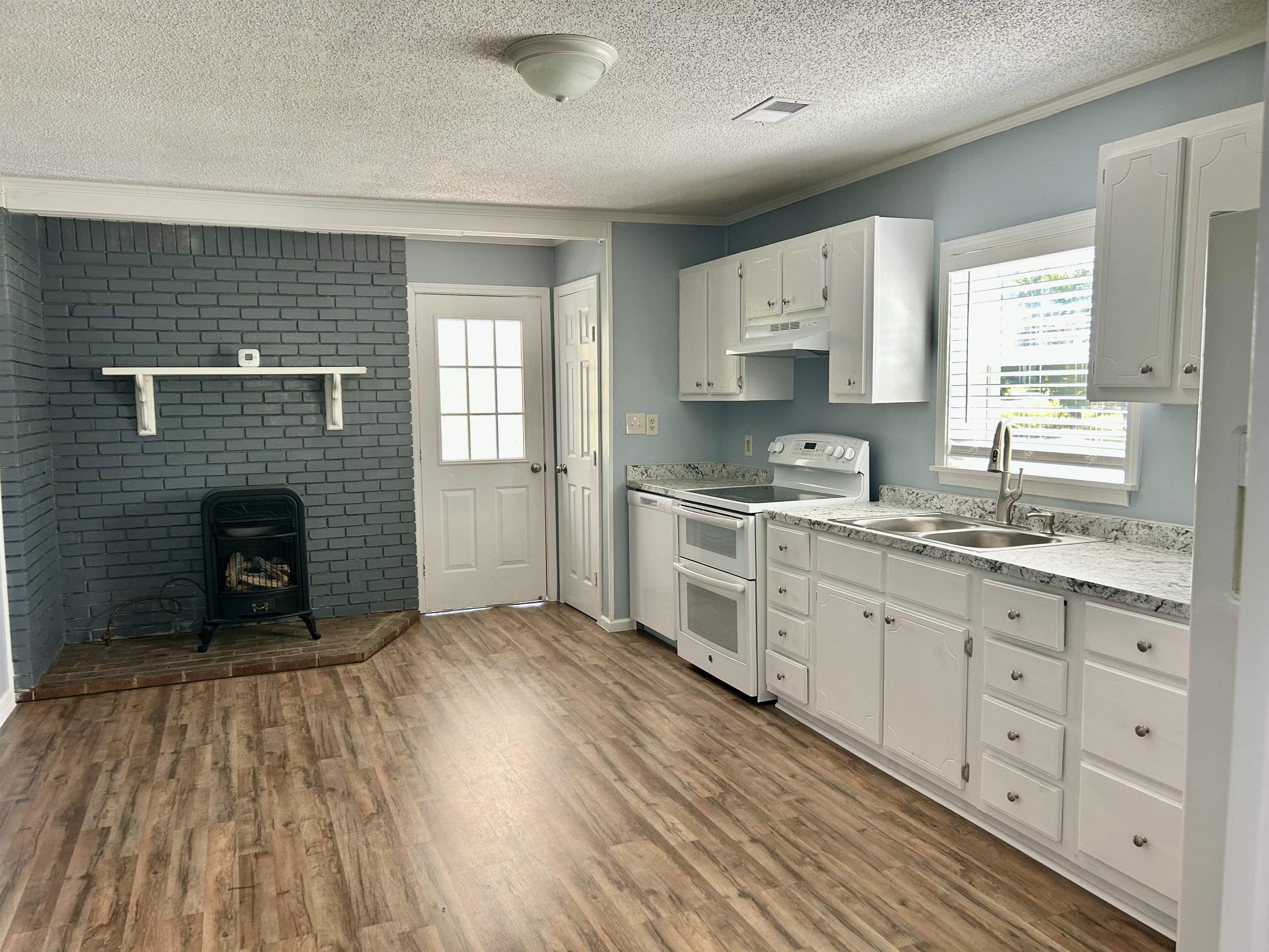 622 Bluebird Hill Road Ripley, TN 38063 - Photo 3 of 14 Kitchen featuring white appliances, light countertops, a wood stove, light wood-style flooring, and a textured ceiling