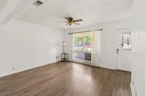 an empty room with wooden floor a ceiling fan and windows