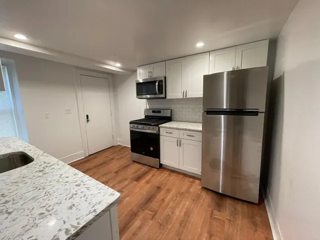 a kitchen with granite countertop a refrigerator a sink dishwasher and a stove with wooden floor