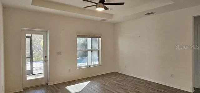 an empty room with wooden floor fan and windows