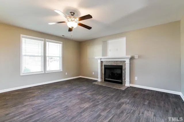an empty room with windows a fireplace a ceiling fan and wooden floor