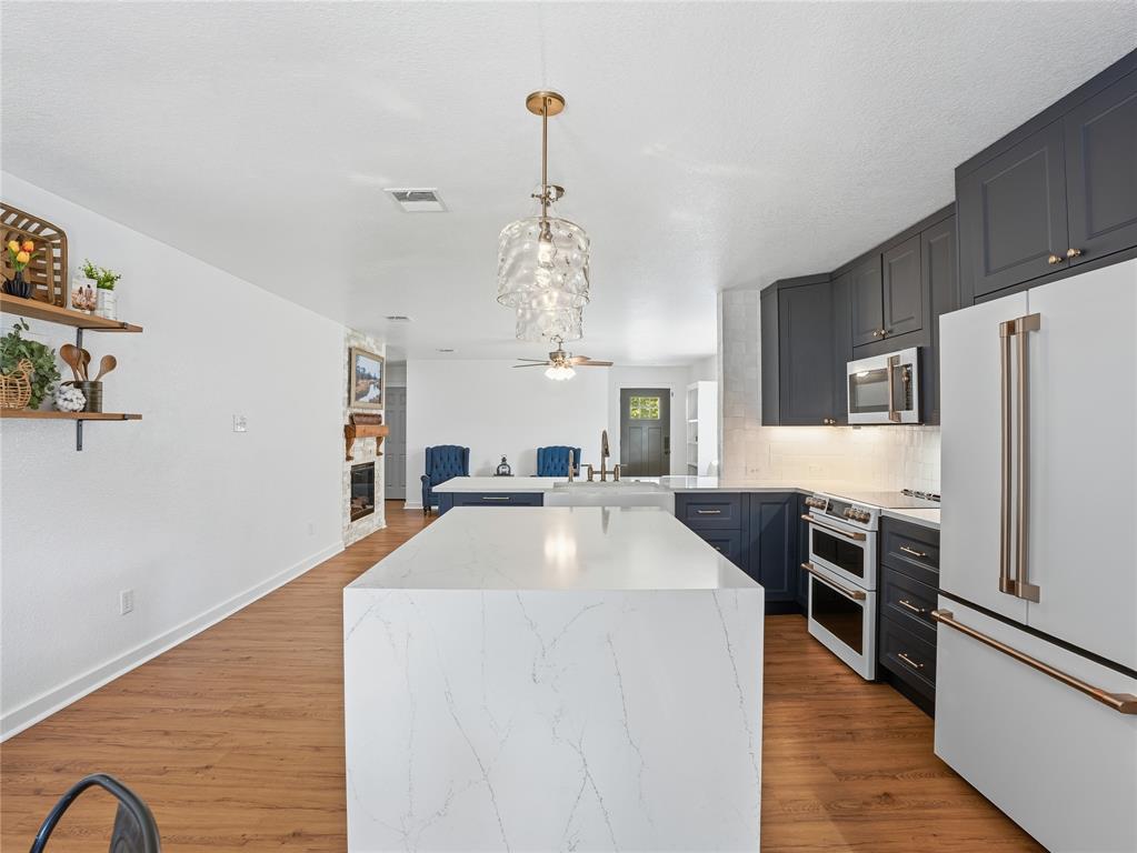 12724 Carpenter Lane Rhome, TX 76078 - Photo 12 of 37 Kitchen featuring a large waterfall island with a light-toned countertop, dark blue cabinetry, stainless steel appliances, and wood-finish flooring