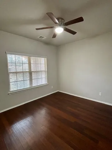 an empty room with wooden floor chandelier fan and windows