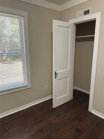an empty room with wooden floor closet and windows
