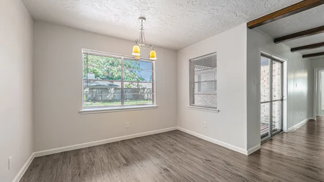 a view of an empty room with wooden floor fridge and a window